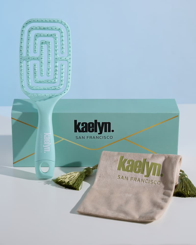 Mint brush leaning on a mint gift box next to a cream drawstring pouch printed with kaelyn. San Francisco, on a light blue background.